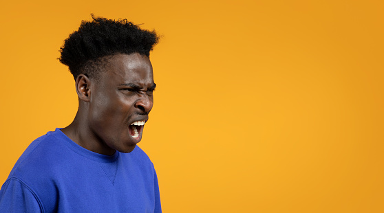 Photo of emotional screaming young black man with closed eyes standing isolated over colorful yellow studio background, closeup shot, panorama with copy space. Human emotions, facial expression