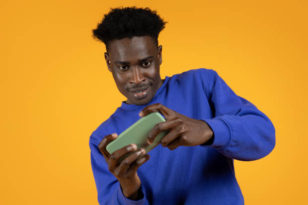 istock Cheerful black guy using cell phone, playing games, yellow background 1862922420