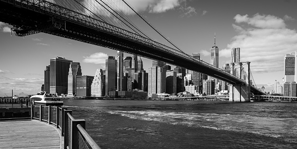 Black and White Stitched Panorama of Statue of Liberty and Manhattan Lower East Side Financial District, Brooklyn Bridge, World Trade Center and Blue Sky with Clouds Reflected in Water of East River, New York, USA. Canon EOS 6D (Full Frame censor) DSLR and Canon EF 24-105mm f/4L lens. 3:1 Image Aspect Ratio.