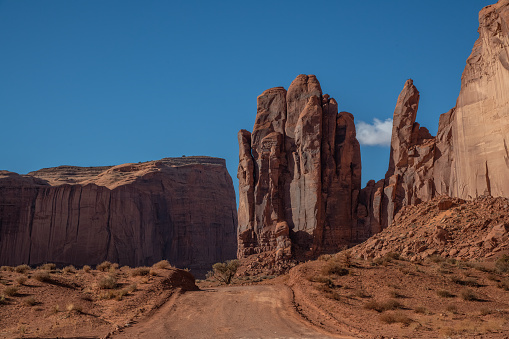Dirt road through Tall spires and mesas of rich dark red rugged mountains near Monument Valley in Arizona and Utah of western USA in North America. This is part of the Navajo Nation in USA.  Nearest cities are Phoenix, Arizona, Salt Lake City, Utah, Denver and Durango, Colorado.