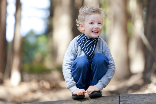 positive smiling boy sitting at the log in the woods