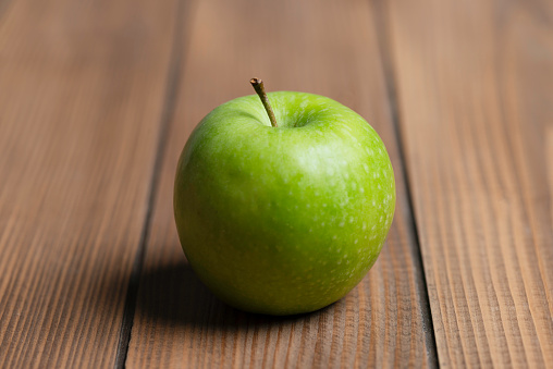 One green apple on wooden table.