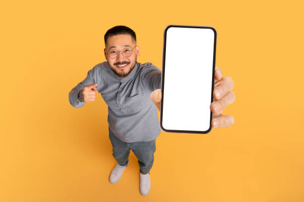 istock Check This. Smiling Asian Man Pointing At Big Blank Smartphone In Hand 1862957739