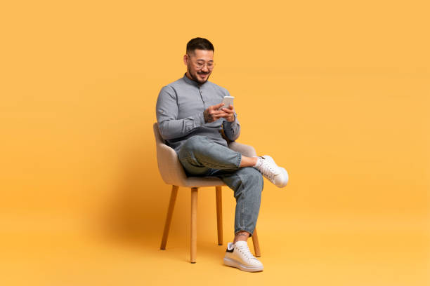 istock People And Technology. Smiling asian man using smartphone and sitting on chair 1862957746