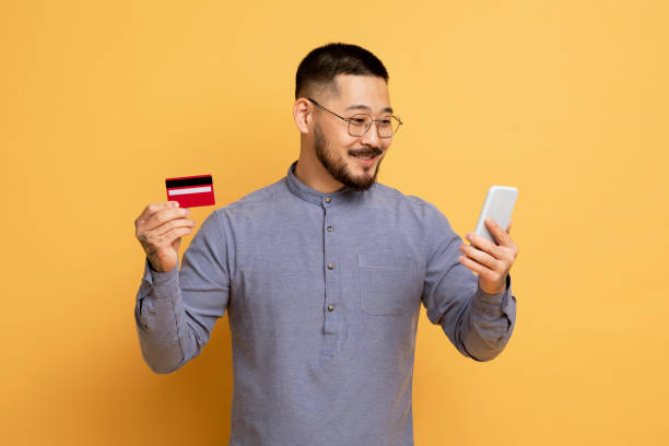 istock Mobile Payments. Smiling Handsome Asian Man Using Smartphone And Credit Card 1862958319