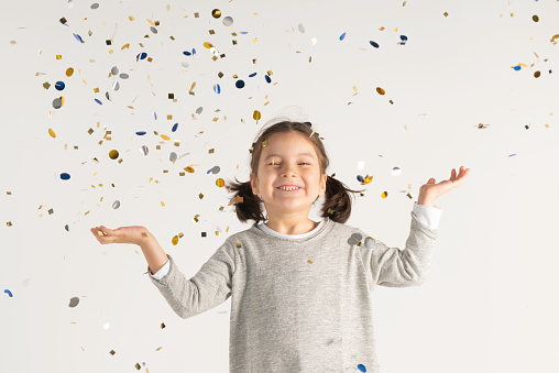 Caucasian girl is standing under confetti falling down and is looking up white closed eyes in front of white background.