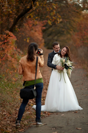 female wedding photographer taking pictures of the bride and groom on the wedding day in autumn