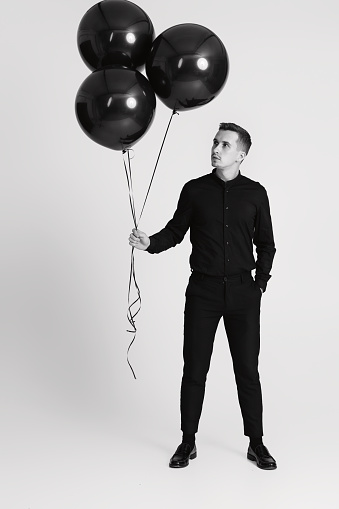 elegant caucasian man with bunch of black air balloons on white background. black and white