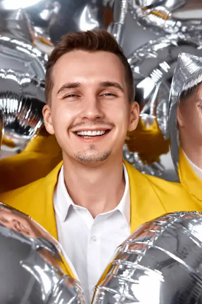 Photo of man in yellow jacket with a lot of silver air balloons
