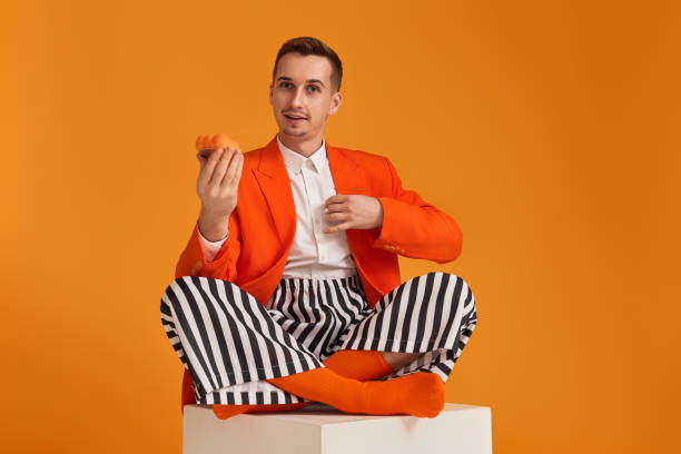 istock young man in orange jacket and striped pants holding cupcake 1863021316