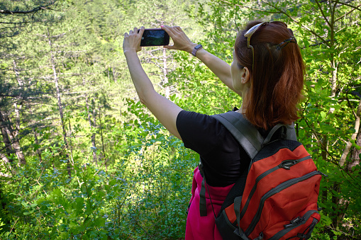 Young woman hiker taking photo with smart phone at mountain green forest. Healthy lifestyle concept.