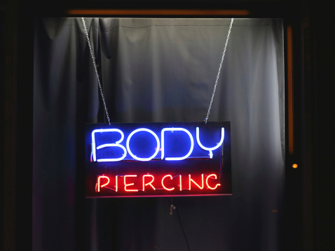 A neon body piercing sign.  The words are expressed as all-capitals.