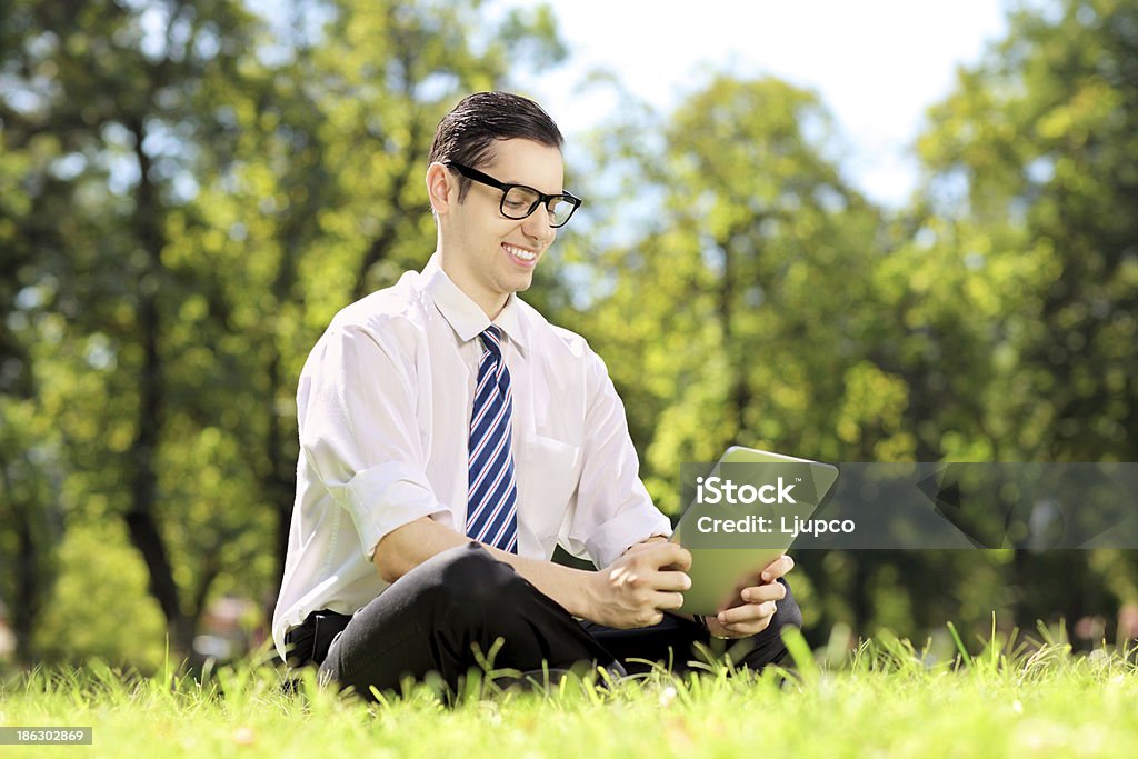 Jovem empresário com óculos, trabalhando em um tablet no parque - Foto de stock de Acessório ocular royalty-free