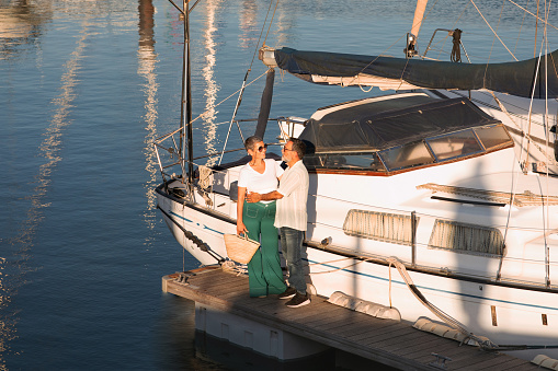 Romantic Sailing Tour. Mature Sailboat Owners Couple Hugging Posing Near Yacht At Dock Outdoors. Spouses Enjoying Summer Vacation Together Posing At Sailboats Park At Seaside. Full Length Shot