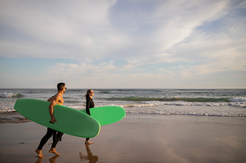 Summer Activities. Happy Young Couple Carrying Surfboards Walking Along Shoreline, Cheerful Athletic Male And Female Surfers Having Fun On The Beach, Enjoying Surfing Together, Copy Space