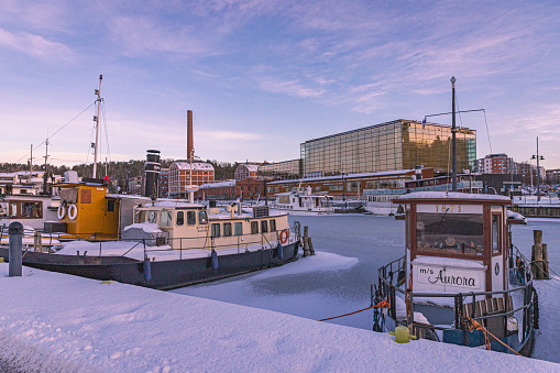 Lahti, Finland. December 17th, 2023. Old steam ships anchored in a frozen lake, in the background sibelius concert hall and old factory.