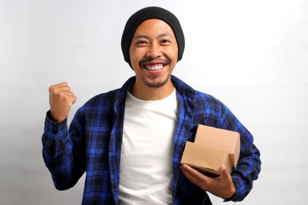 istock Happy Asian customer raises his arm in a YES gesture while holding package parcel cardboard box 1863084574