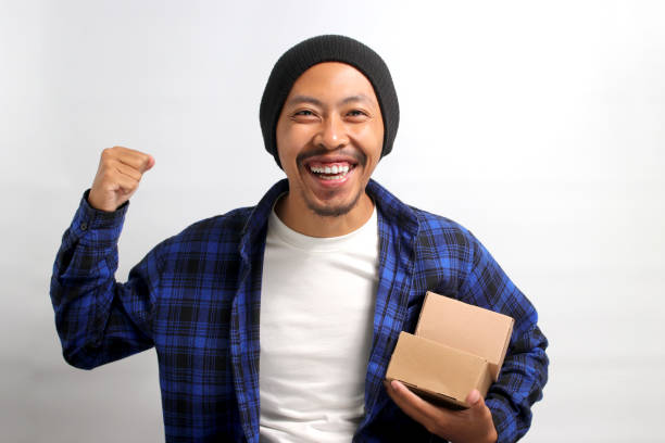 istock Happy Asian customer raises his arm in a YES gesture while holding package parcel cardboard box 1863089283