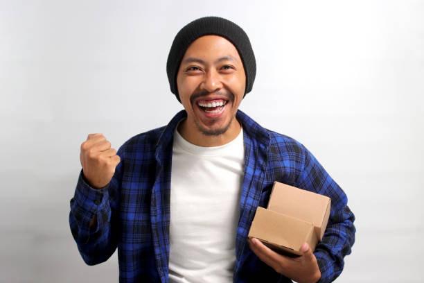 Happy Asian customer raises his arm in a YES gesture while holding package parcel cardboard box