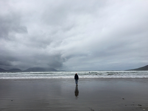 A lone female standing in front of the ocean on a grey moody day on the coast of the Aran Islands, located just off Galway and Doolin on the Irish mainland