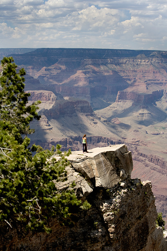 A lone woman standing out on a ledge  overlooking the Grand Canyon. The Grand Canyon has been carved, over millions of years, as the Colorado River cuts through the Colorado Plateau.The canyon offers stunning panoramic views, unique geological formations, and a sense of wonder at the natural world.Geologists debate the age of the canyon itself—it may be between 5 million and 70 million years old.