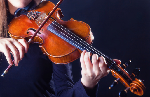 Playing the violin. Musical instrument with performer hands on dark background.