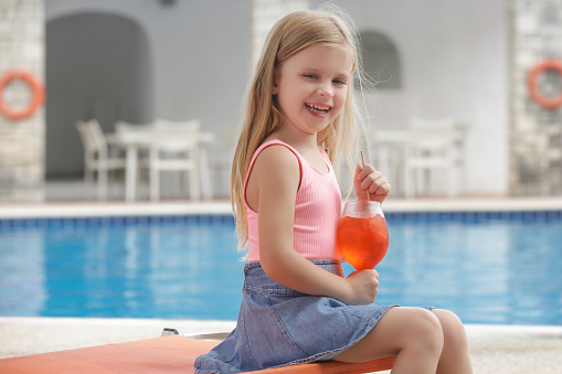 Adorable little girl having refreshment drinkby the poolside, hydratation and healhy diet during hot summer days