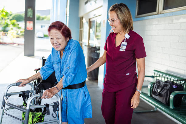 Home caregiver assisting elderly patient with transfer gait belt while walking outside medical complex