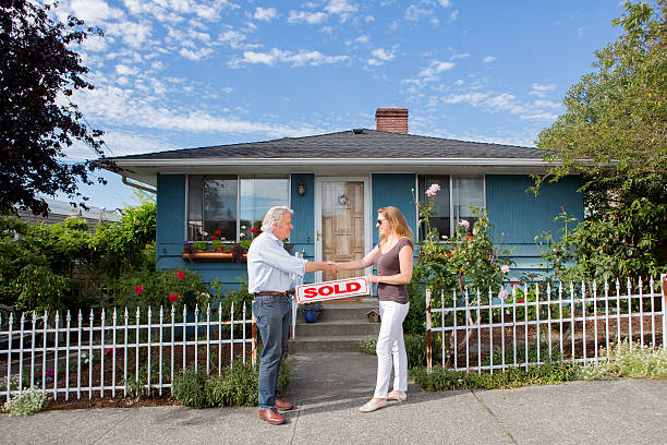 Real Estate Agent and Buyer Shake Hands In Front of Sold Home. An older man and a younger woman shake hands over a "Sold" sign to celebrate a successful home sale. door to door salesperson photos stock pictures, royalty-free photos & images