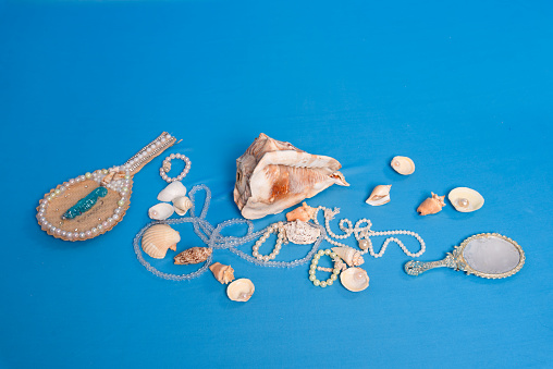 Several sea shells, necklaces and mirror scattered on the blue studio floor. Tribute to iemanja.