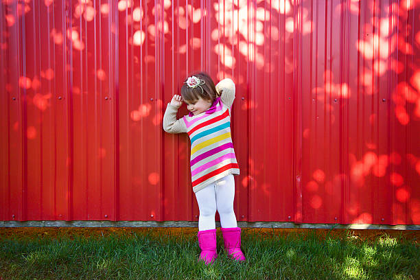 Journey in nature. Adorable happy girl throwing the fallen leaves up, playing in the autumn park. Little blonde hair and blue eyes girl smiling expression. Girl in polka dot red dress and boots