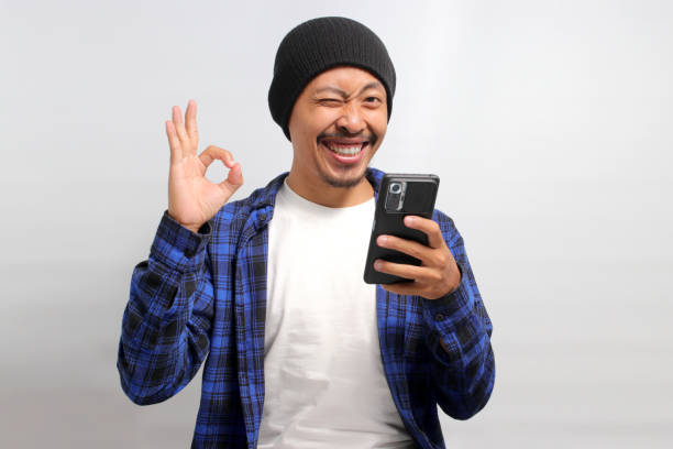 istock Asian man makes OK gesture while holding his phone 1863256168