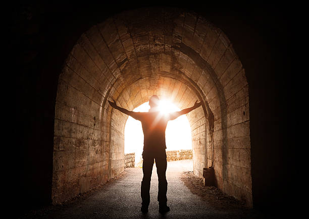 Man stands inside of old dark tunnel with shining sun Man stands inside of old dark tunnel with shining sun in the end light at the end of the tunnel photos stock pictures, royalty-free photos & images
