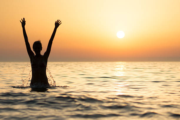 istock girl jumping into sea at sunset 186332335