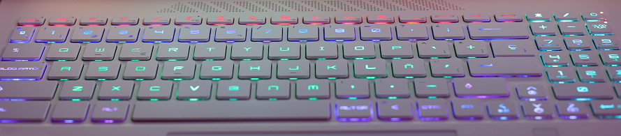 Colorful illuminating neon çkeyboard from a workplace laptop computer in low light scene.