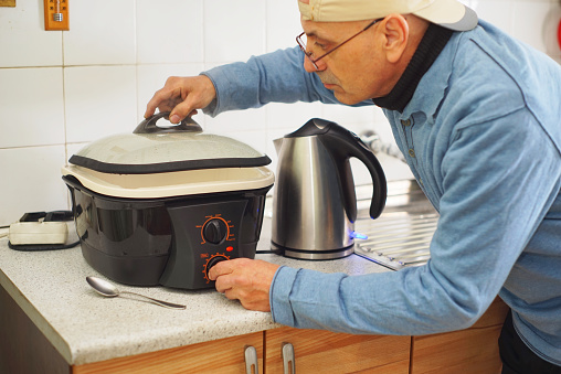 Close up view of a man preparing lunch on multi functional electric cooking pot and heating water on electric kettle.