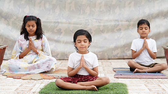 Meditating With Eyes Closed, Charming little girl doing serious yoga meditation in studio with her siblings.