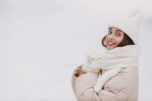 Happy smiling young woman portrait dressed coat scarf hat and mittens enjoys winter weather at snowy winter park