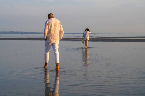 Couple standing in sea water barefoot, wide shot back view