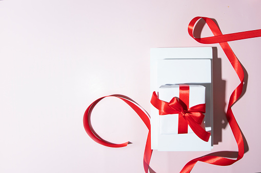 Still life gift giving conposition. White podiums with white gift box and red ribbon on pink background for abstract. Copy space