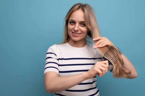 encantadora mujer rubia europea peinando su cabello sobre un fondo azul aislado - mid adult women human skin neat good condition fotografías e imágenes de stock