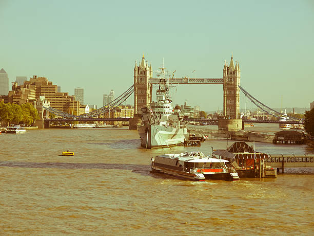 Sunlit image of the iconic Tower Bridge in London, with river traffic and distant urban skyline. The scene captures the essence of a bustling yet historic metropolitan city during a golden hour.