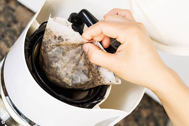 Removing old coffee filter Horizontal photo of female hand pulling out used coffee filter, from coffee machine, with stone counter top in background coffee filter stock pictures, royalty-free photos & images