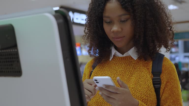 Black women with short, curly hair check-in via automatic machines by themselves in the airport to travel or study abroad.