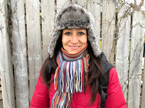 An attractive woman, smiling and wearing a fake fur hat and a red coat and colourful scarf.
