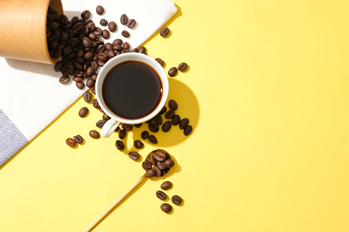 Coffee beans poured from a cup, a cup of black coffee on a yellow background. Coffee contains caffeine which prevents drowsiness. Free space for design.
