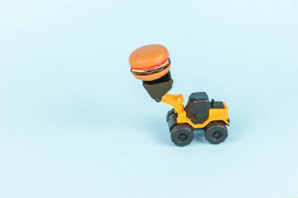 istock A bulldozer carrying a hamburger on a blue background. 1863627288