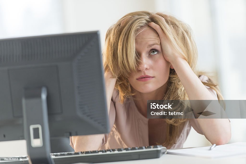 Frustrated Businesswoman With Hands In Hair At Office Desk Young frustrated businesswoman with hands in hair looking up at desk in office Frustration Stock Photo