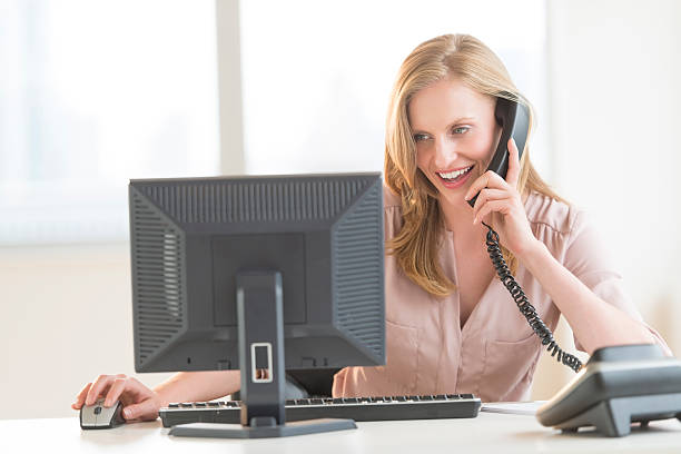 istock Businesswoman Using Computer While Conversing On Landline Phone 186372487