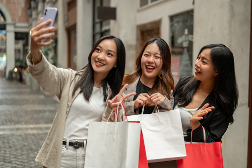 Young cheerful and pretty Asian girls are taking selfies with a smartphone while enjoying their shopping day in the city together. Friendship and lifestyle concepts